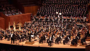 Simone Young stands with arms to the side in front of the Sydney Symphony Orchestra with a full choir insider the Concert Hall