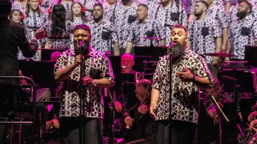 The Signature Choir in matching black and white designed shirts sing in front of an orchestra