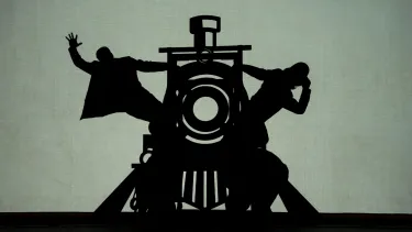 A silhouette of two people hanging from either side of a characterisation of a train.