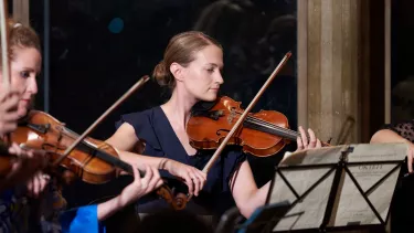 Two violin players stand in front of an art deco wall