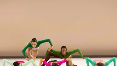 A group of five dancers in colorful leotards performing an artistic formation on stage.