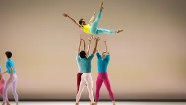 A dancer is elevated above four dancers, who are lifting the dancer.