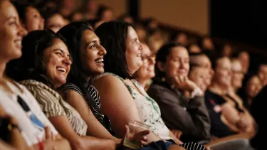 A diverse group of audience members smile in the audence.