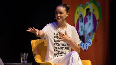 A young woman with one hand on her chest gesture to the audience.