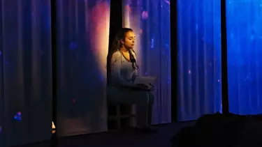 A young lady meditating in a spotlight.