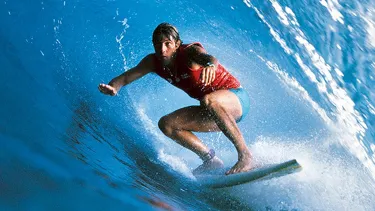 A man in a red vest and blue shorts surfs through the barrel of a wave with his arms out in front.