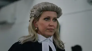 A woman wearing a traditional barrister's wig and a black gown, with an elegant white collar and large earrings.
