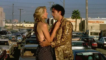 Nicolas Cage and Laura Dern's characters embrace on top of a car on a busy road surrounded by traffic.