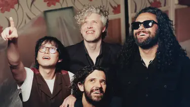 Four men smile and point at something behind the camera.