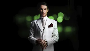 A man in a white suit stands in front of a green background.