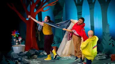 Three performers hold up the back of each others raincoats to create the illusion of flying with capes.