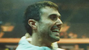 A white man in a white jacket looks over his shoulder smiling