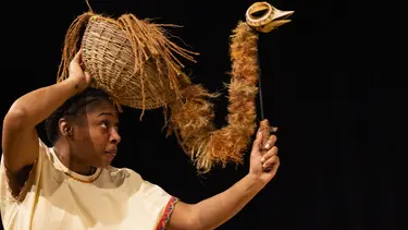 A performer holds a long necked bird puppet above her head.