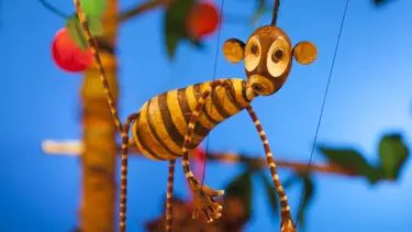 A monkey puppet hangs in the air with it's tail wrapped around the branch of a fruit tree.