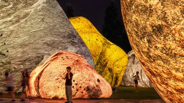 A series of different coloured inflatable rock structures tower above people in a park.