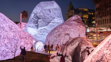 People stand within a maze of large inflatable glowing rocks. Buildings are visible in the background.