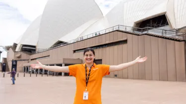 An Opera House staff member stands arms outstretched in front of the Opera House sails.