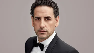 A man with dark curly hair looks at the camera wearing a tuxedo