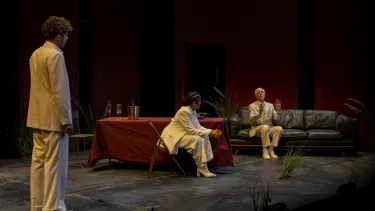 Two actors dressed in white sit across each other while somebody watches on.