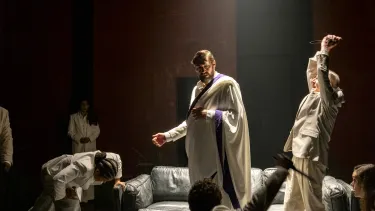 A figure stands in the light as he is surrounded by people holding knives.