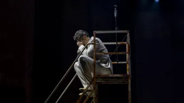 A man in white holds his head in his hands sat on a step.