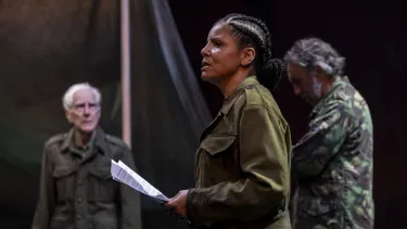 Three actors stand dressed in military camouflage.