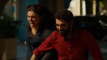 A woman in a dark blue outfit and a man in a red shirt are running together, both appearing engaged in a lively moment.