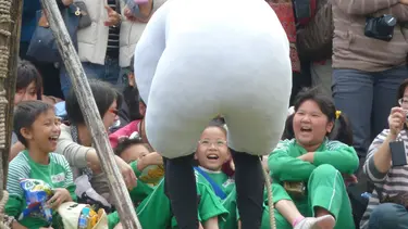 A performer in a sheep suit is standing in front of a group of laughing children.