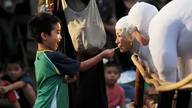 A smiling child feeds a performer in a sheep suit.