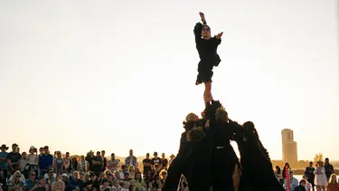 A large crowd watch as a performer is balanced on top of a group of performers.