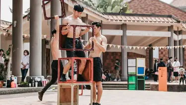 Two performers place cubes on top of another circus performer.