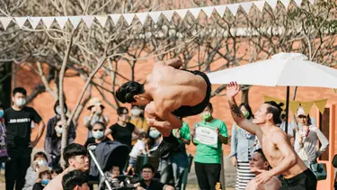 A performer flips through the air over the top of scaffolding like cubes. Other performers are crouched on either side.