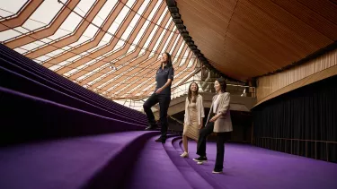 Tour guide leads two people up purple stairs in the Sydney Opera House