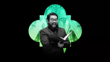 Man with a beard in a black suit sings with a cathedral as the background