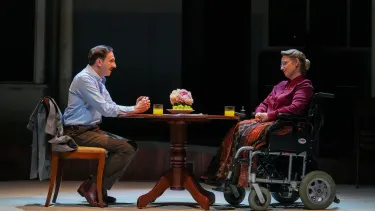 Man in a blue shirt sits as he pleads with a woman in a wheelchair.