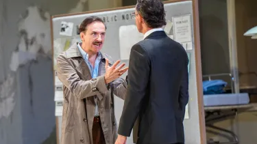 A man in a khaki coat shouts with both hands up at another man in a suit.