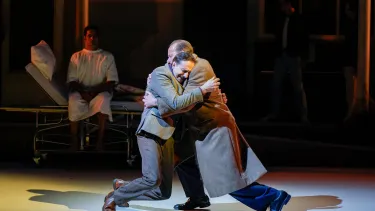 Two men in coats embrace on stage.