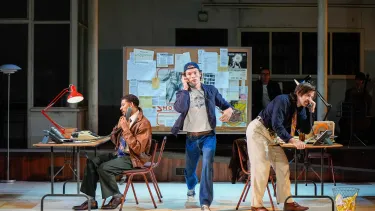 Two men on tables split the side speak on the phone while a man runs down the middle on a mobile phone.