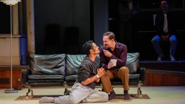 Two men smile at each other closely with a tub of ice cream.