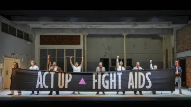 Eight men stand on stage holding an Act Up Fight Aids banner.