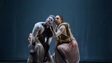 A female dance holds the chin of a male dancer.