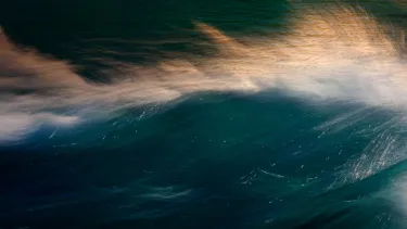 The surface of a dark body of water with light reflected of gentle waves and wind creating soft spray of whitewater.