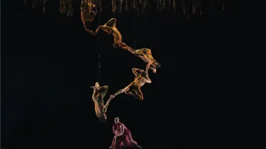 Five dancers create a connect spiral midair above a woman in red.