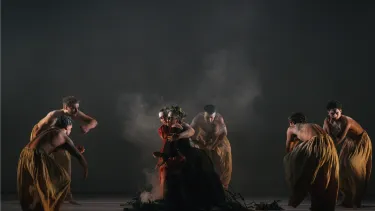 Five dancers surround two women dressed in red.