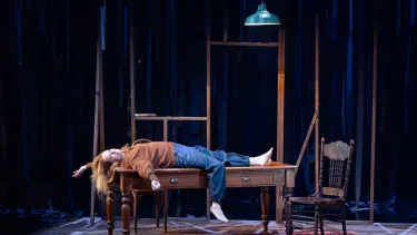 A red-haired woman in an orange top and denim jeans is laying on top of a table.