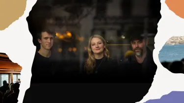 Three people sitting in a warmly lit setting behind a window, smiling softly.