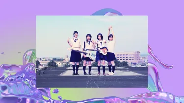 Four girls stand side by side. Two are holding guitars and all are holding up peace signs.