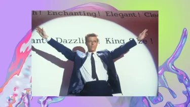 David Bowie's character Vendice Partners stands in front of a wall illuminated by a spotlight.