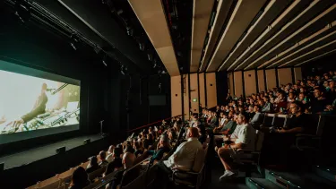 People seated in tiered rows viewing a film on a large screen.