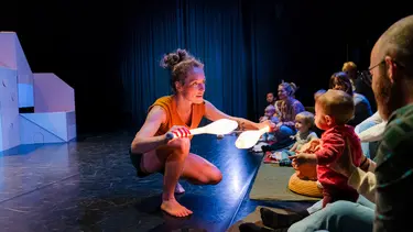 A woman is crouched at the front of the stage holding up two glowing sticks to a young child.